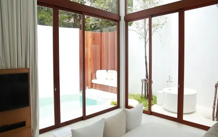 Blick durch große Glasschiebetüren auf eine private Terrasse mit Pool und Badewanne im Freien.