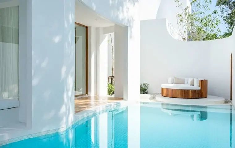 Türkisblauer Pool vor der weißen Gebäudewand mit einer runden Liegeinsel.
