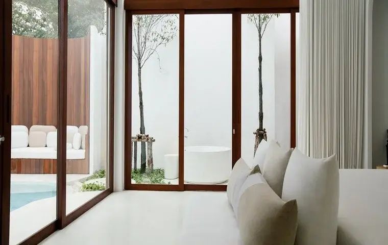 Blick aus dem Wohnbereich durch bodentiefe Fenster auf einen Innenhof mit Badewanne.