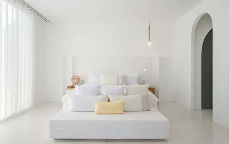 Minimalistisch gestaltetes Hotelzimmer mit weißem Doppelbett und hellen Kissen.