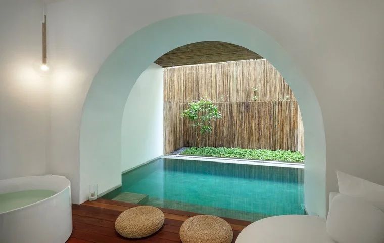 Privater Pool einer Villa mit Rundbogen, Holzterrasse und Sitzkissen vor einer Bambuswand.