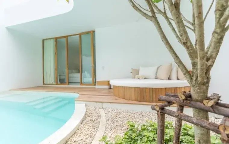 Holzterrasse mit rundem Tagesbett neben einem Pool und verglasten Türen zum Zimmer.