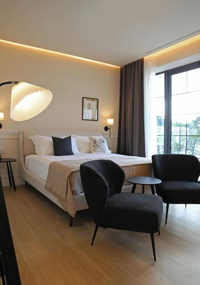 Modernes Hotelzimmer mit Doppelbett, zwei dunklen Sesseln und indirekter Beleuchtung.