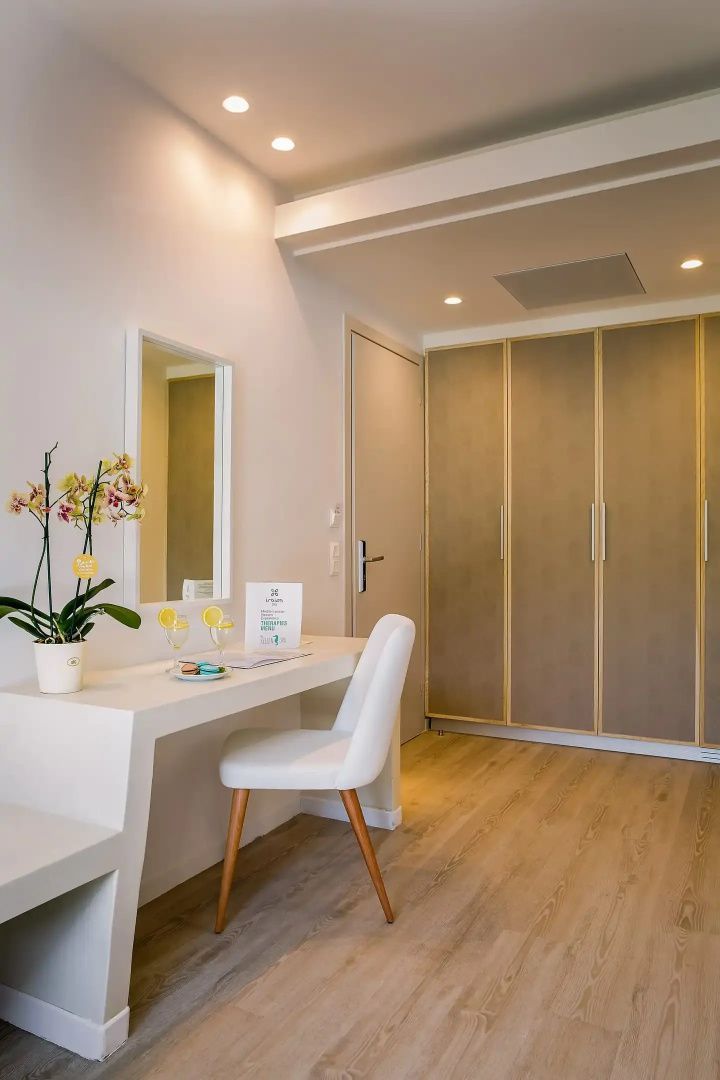 Schreibtischbereich im Hotelzimmer mit weißem Stuhl, Wandspiegel und Schrank.