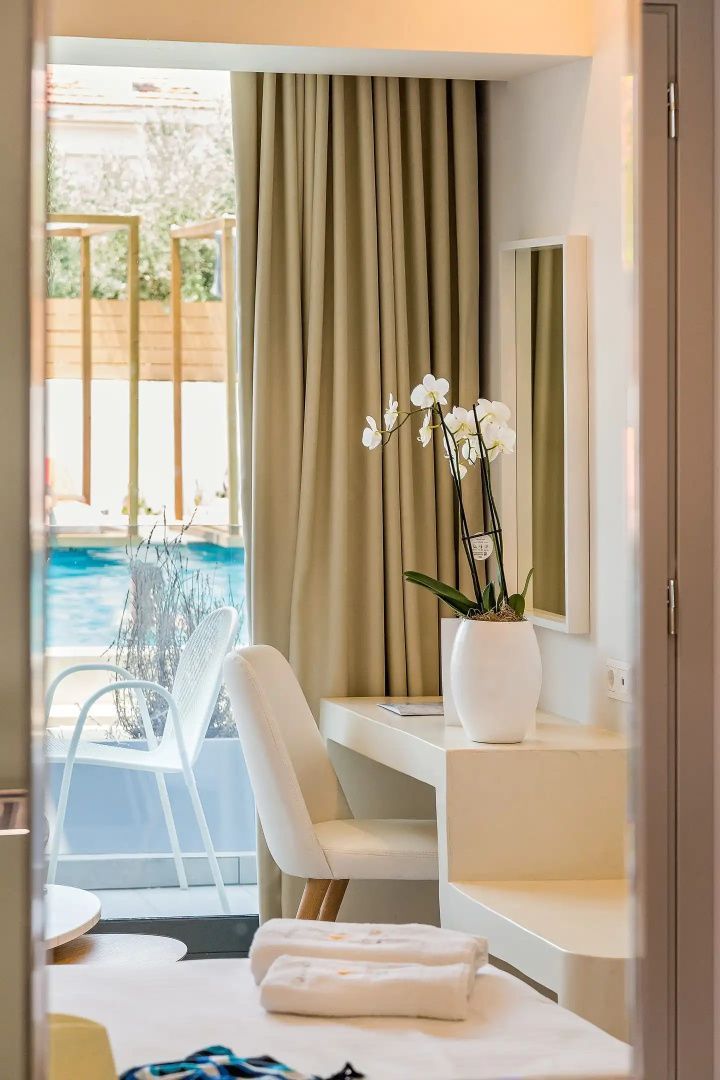 Heller Schreibtisch mit weißem Stuhl und Orchidee sowie Blick auf den Außenpool.