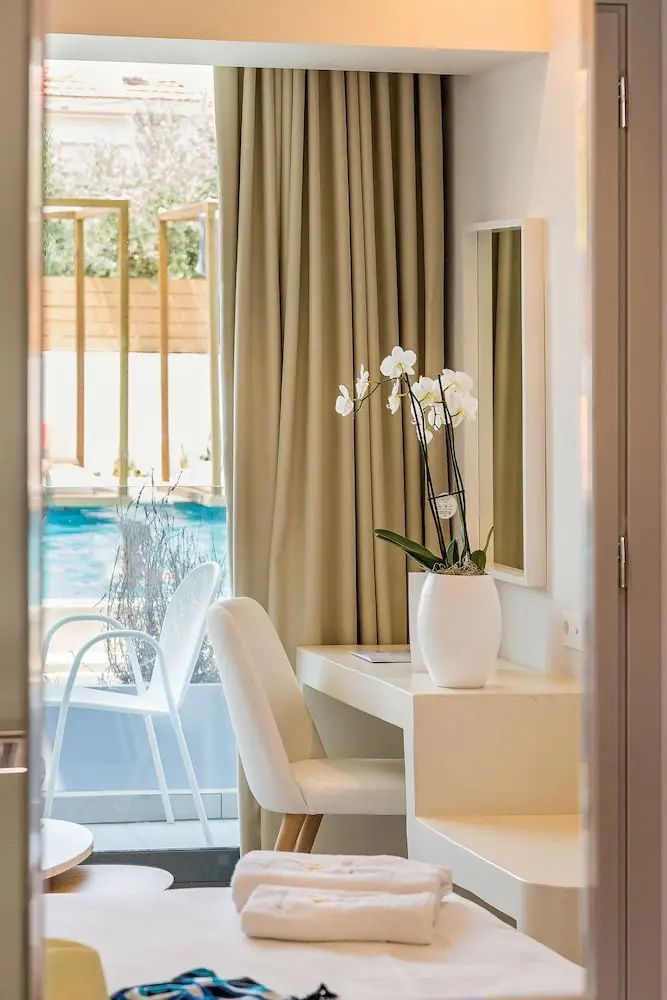 Schreibtisch mit weißer Orchidee im Hotelzimmer und Blick durch das Fenster auf den Außenpool.