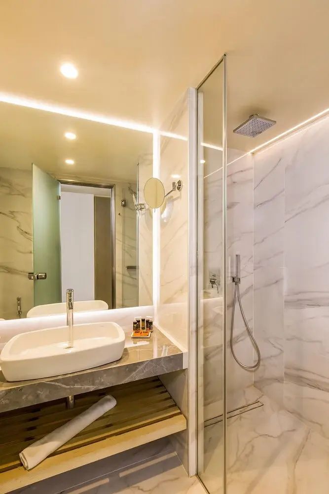 Badezimmer mit Marmorwand, beleuchtetem Spiegel und Glasdusche.