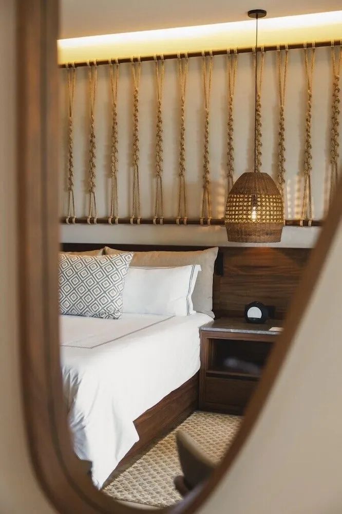 Doppelbett mit Kissen, Nachttisch und gewebter Lampe vor einer Wand mit Flechtdekoration.
