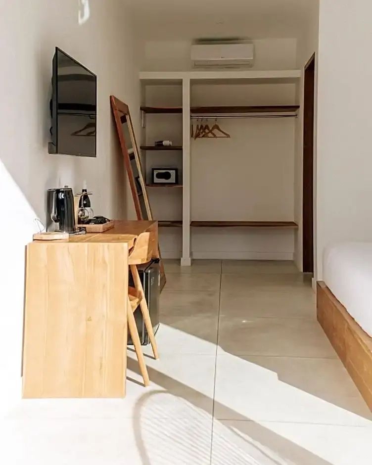 Helles Hotelzimmer mit Schreibplatz aus Holz, Flachbildfernseher und offenem Schrank.