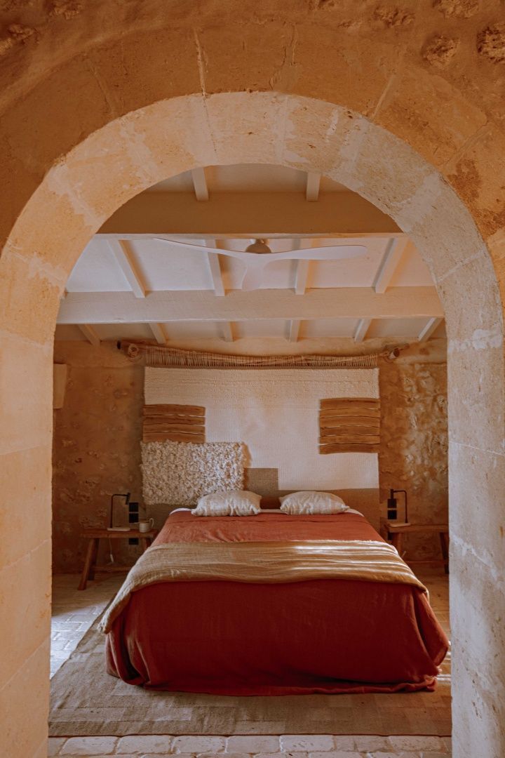 Blick durch einen Steinbogen auf ein Doppelbett mit rotbrauner Decke und Natursteinwand.