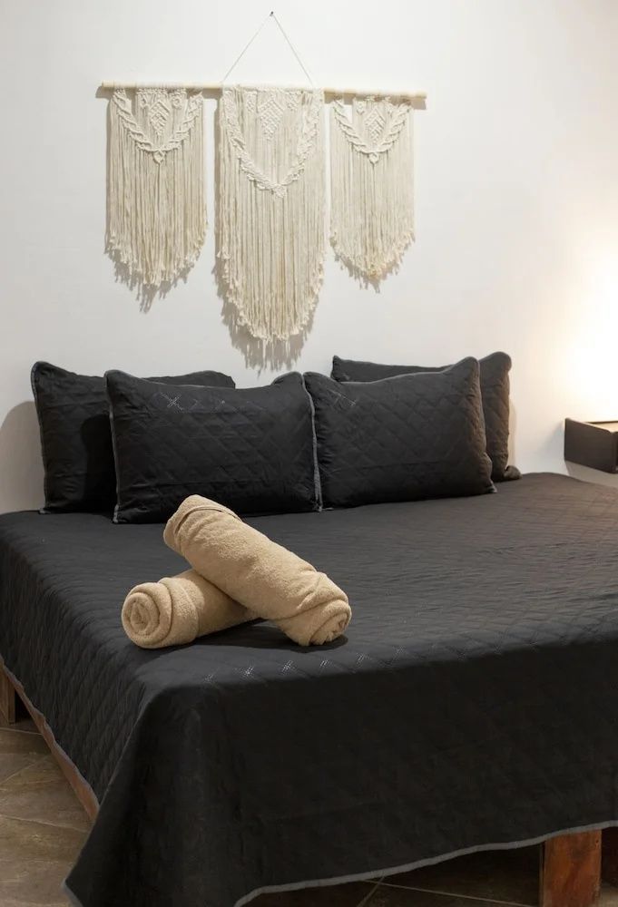 Doppelbett mit schwarzer Bettwäsche, Handtüchern und Wanddekoration aus Makramee.