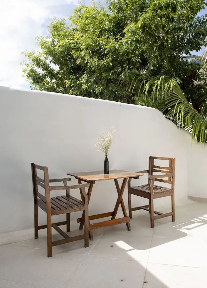 Kleine Holzsitzgruppe auf einer hellen Terrasse vor weißer Wand.