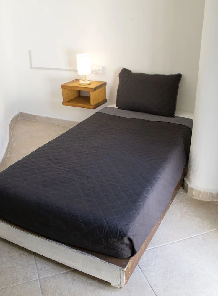 Einzelbett mit dunkler Tagesdecke und hölzernem Nachttisch mit Lampe.