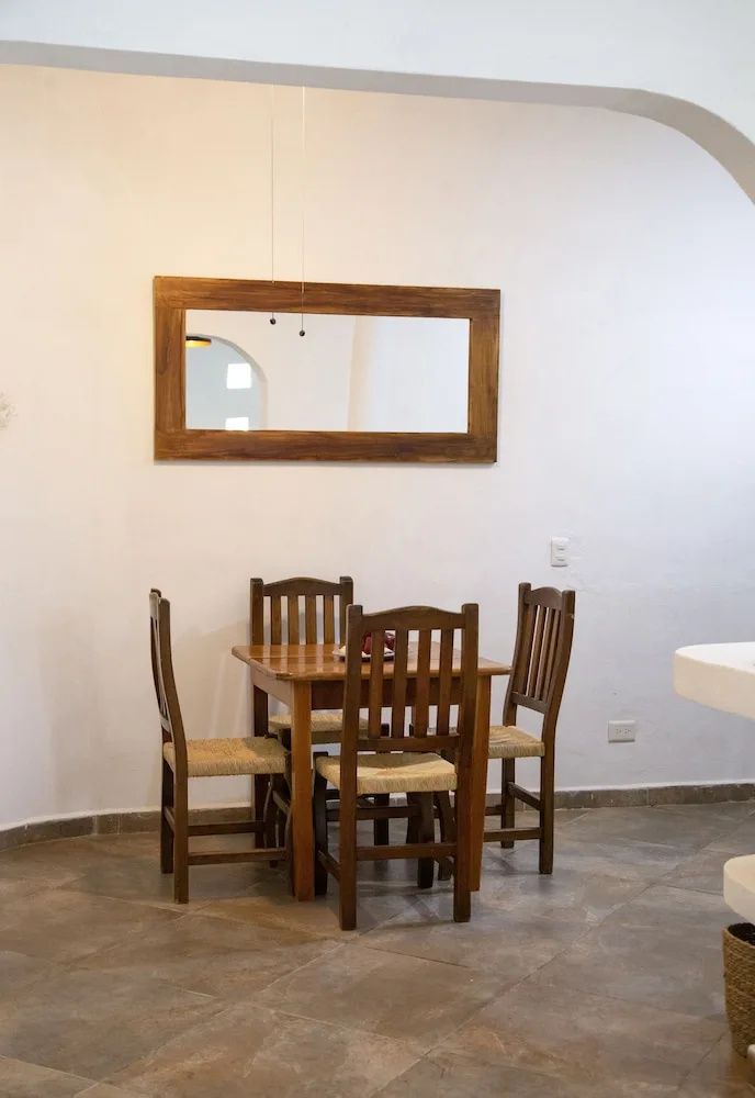 Holztisch mit vier Stühlen und ein großer Spiegel mit Holzrahmen an einer weißen Wand.