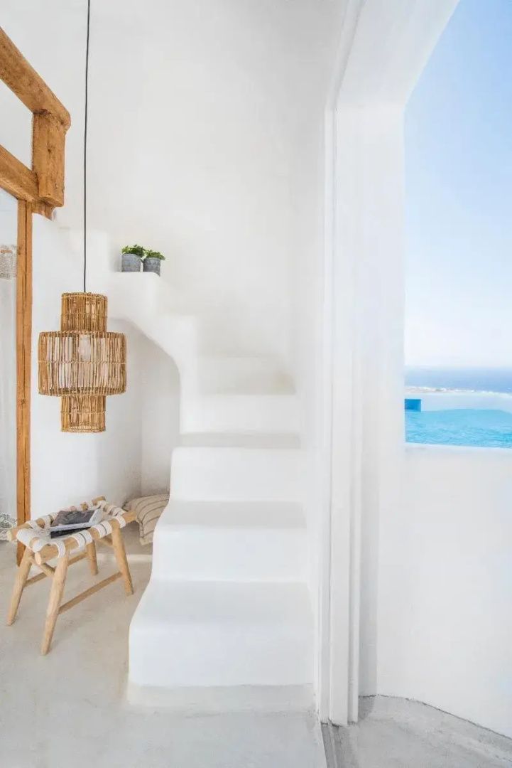 Weiße Treppe im Innenbereich mit geflochtener Lampe und Blick ins Freie auf das Meer.
