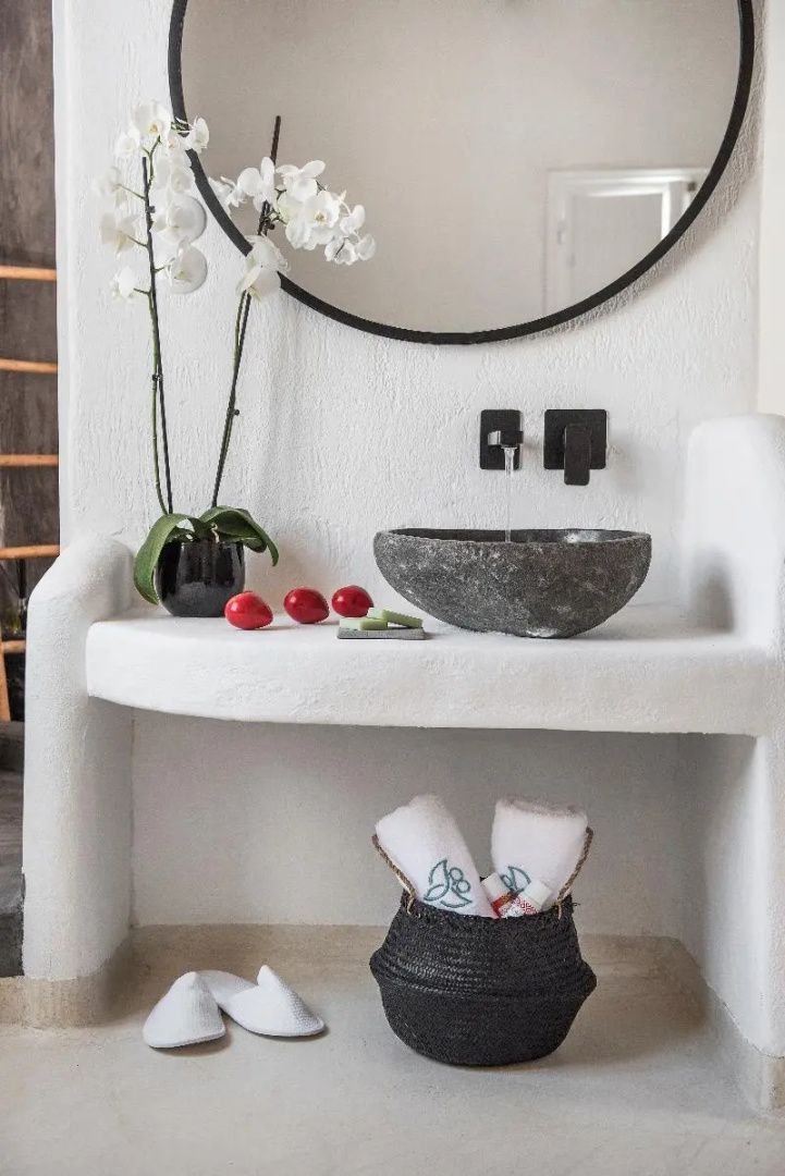 Weißer Waschtisch mit einem Steinwaschbecken, Orchidee und Handtüchern im Korb.