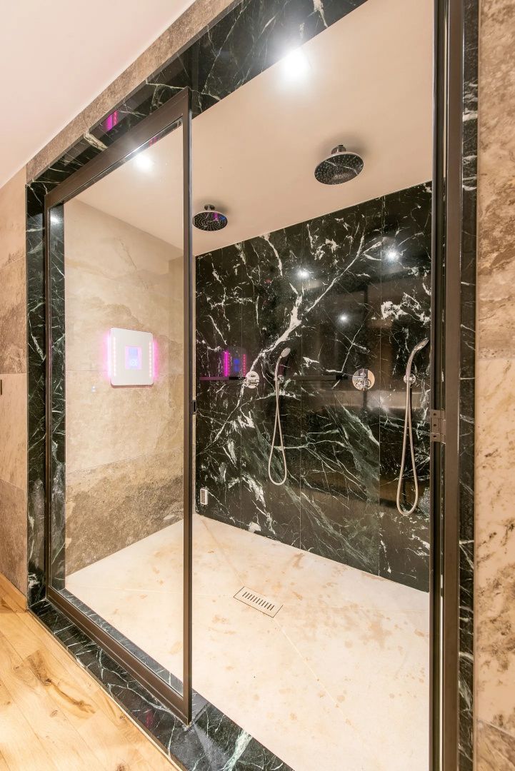 Moderne begehbare Dusche mit dunklem Marmor, Regendusche und Glasfront.