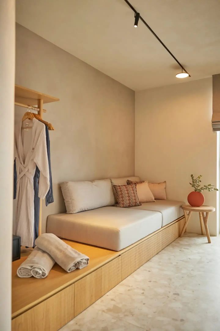 Sitzbereich im Zimmer mit hellem Sofa, Kissen, Holzgarderobe und Bademänteln.