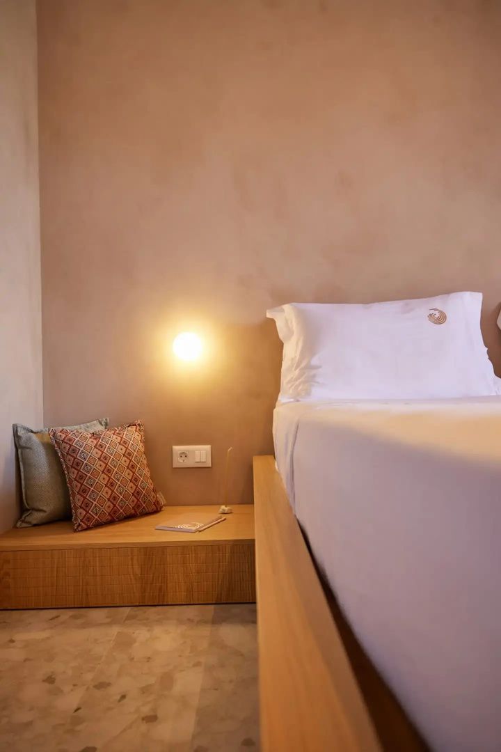 Bett mit weißer Bettwäsche und Kissen neben einer brennenden Wandleuchte.