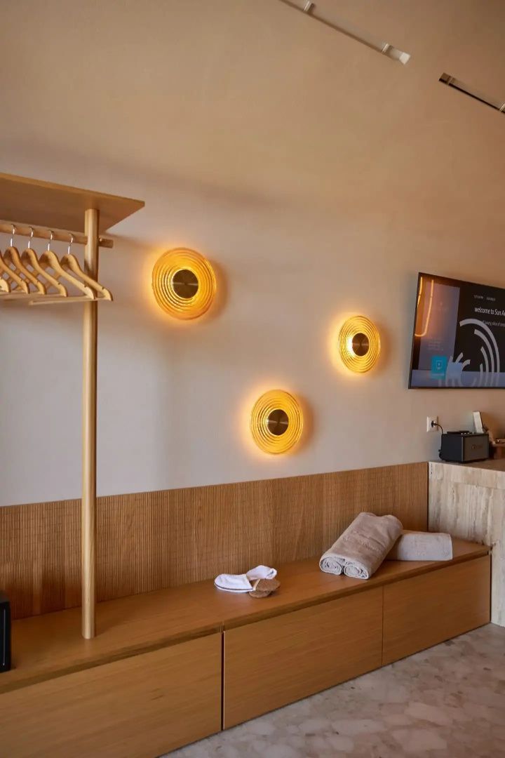 Schlafbereich mit Garderobe, kreisförmigen Wandleuchten und Holzbank mit Handtüchern.