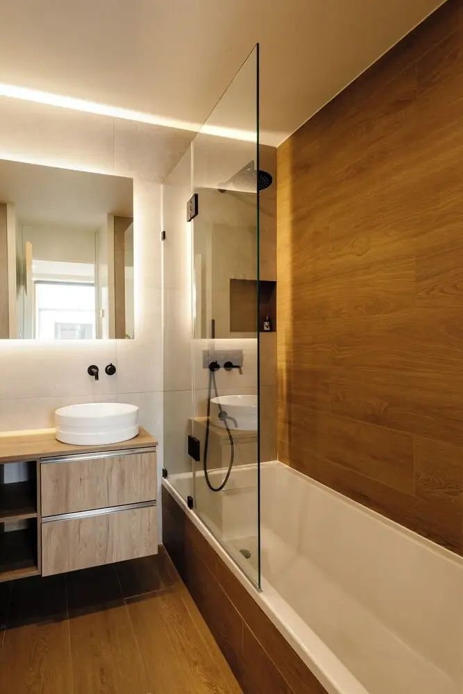 Modernes Badezimmer mit weißem Aufsatzwaschbecken, beleuchtetem Spiegel und Badewanne mit Glaswand.