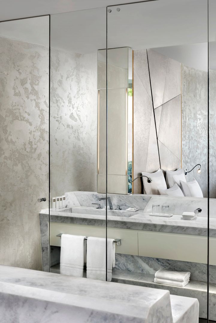 Badezimmerbereich aus Marmor mit Waschbecken und gläserner Abtrennung.