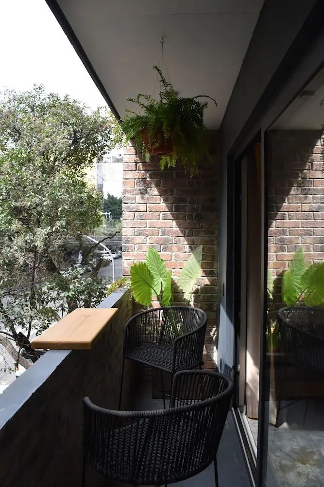 Balkon mit Backsteinwand, schwarzen Stühlen, grünen Pflanzen und Blick ins Grüne.