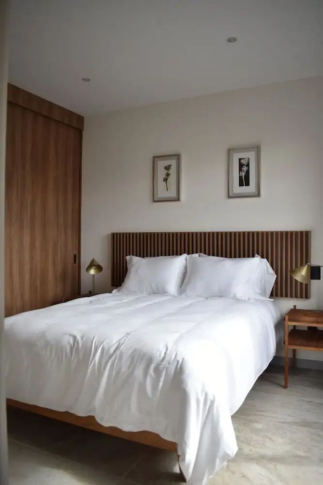 Helles Schlafzimmer mit Holzlamellen am Kopfteil des Doppelbetts und Wandbildern.