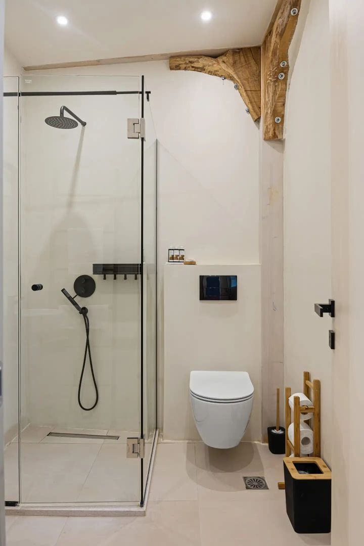 Modernes Badezimmer mit begehbarer Glasdusche, schwarzen Armaturen und wandhängendem WC.