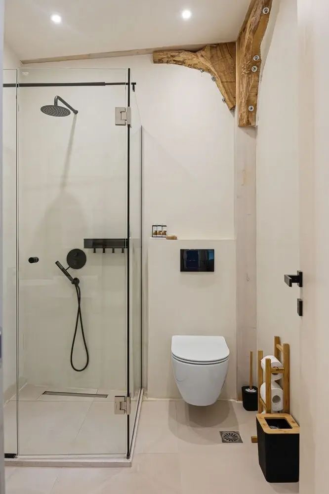 Badezimmer mit bodengleicher Glasdusche, schwarzen Armaturen und wandhängendem WC.