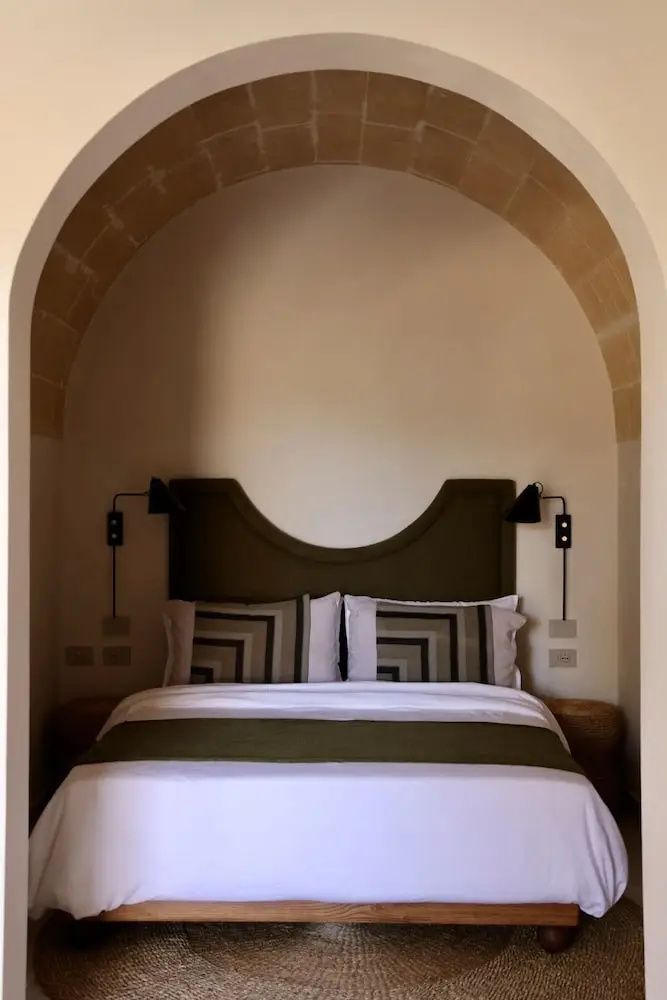 Doppelbett in einer Rundbogennische mit grünem Kopfteil und zweifarbiger Bettwäsche.