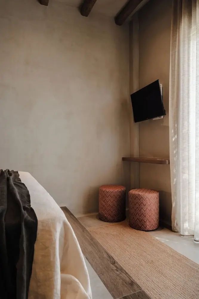 Ecke eines Hotelzimmers mit Fernseher an der Wand, Holzablage und zwei gemusterten Hockern.