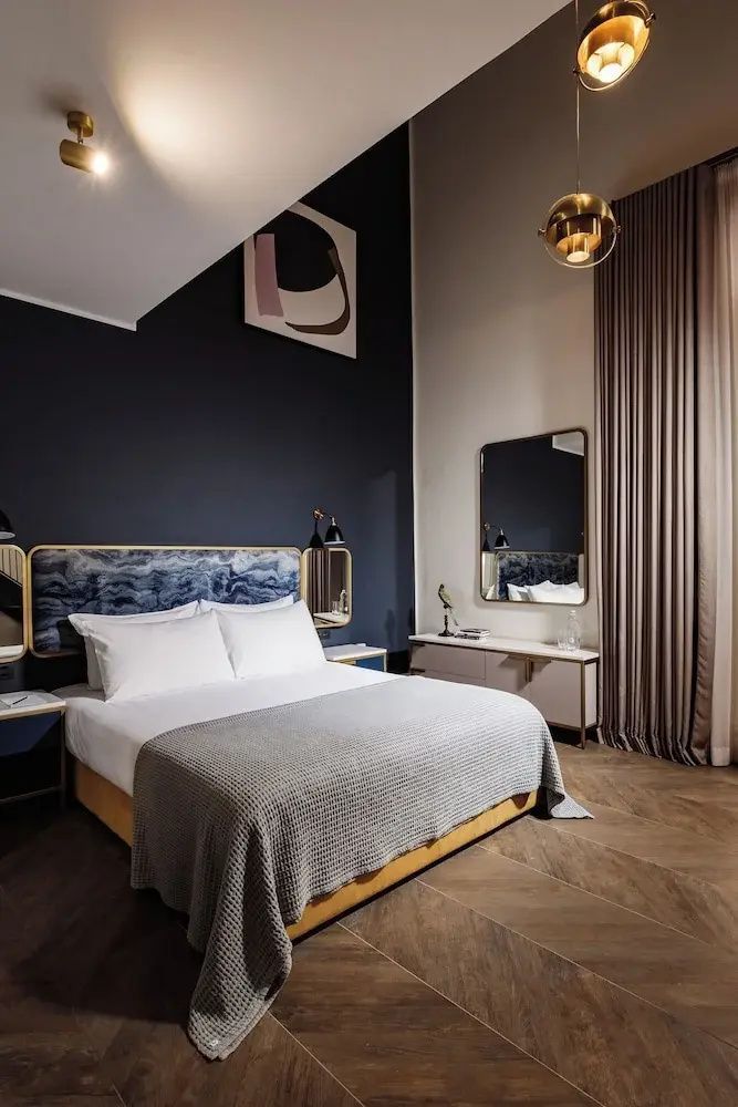 Modernes Hotelzimmer mit Doppelbett, blau strukturiertem Kopfteil und Parkettboden.