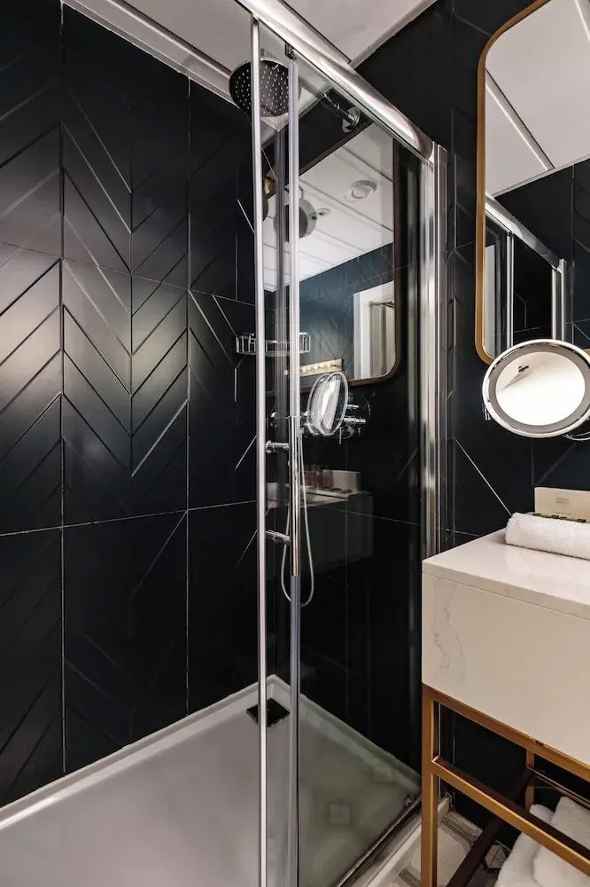 Badezimmer mit dunklen Fliesen im Fischgrätmuster, Dusche und weißem Waschtisch.