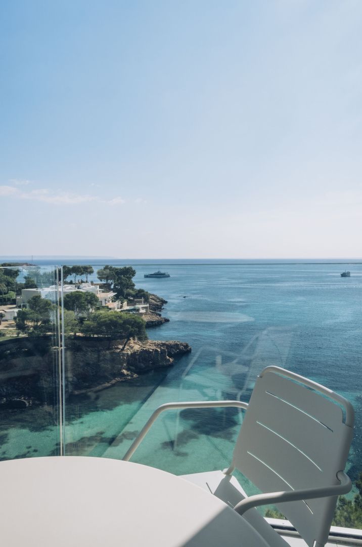 Blick von einem Balkon auf eine Küstenlandschaft mit grünem Bewuchs und türkisblauem Meerwasser.
