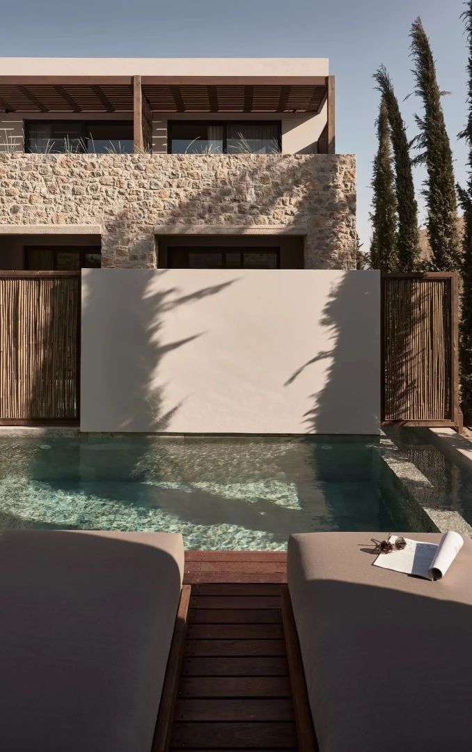 Sonnenliegen am privaten Pool vor einer Natursteinwand und einer weißen Sichtschutzwand.
