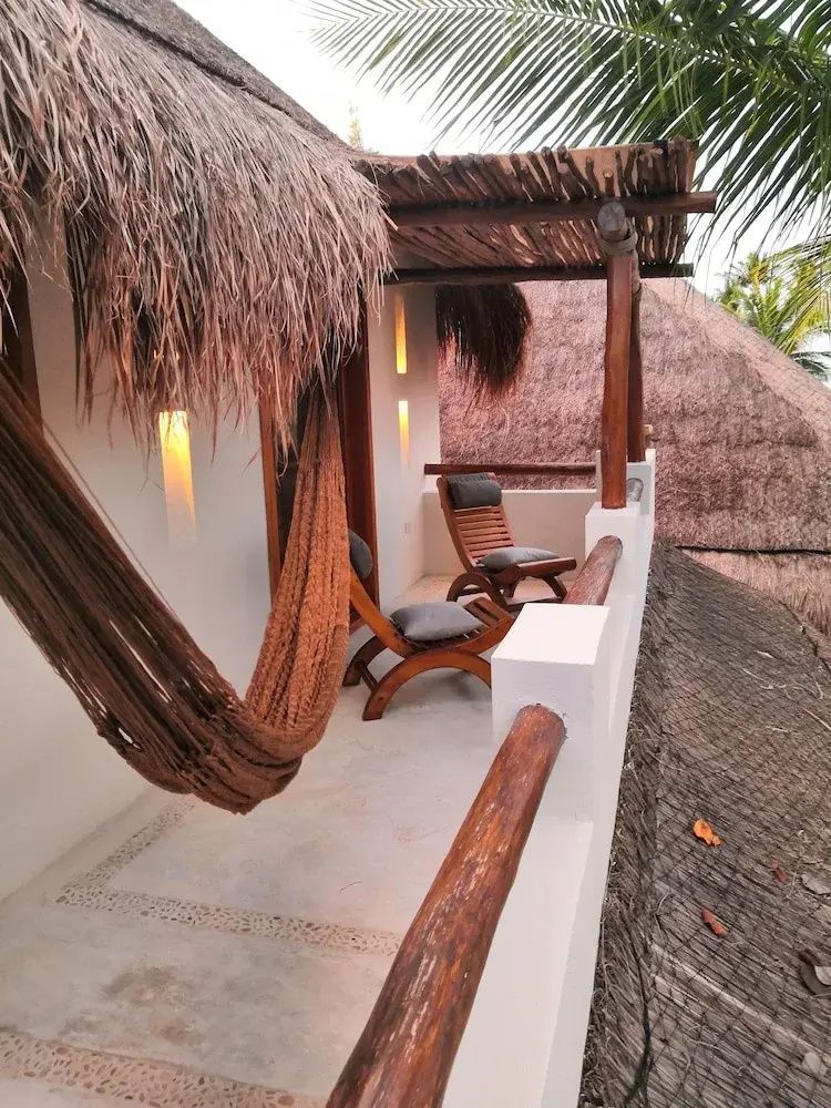 Balkon mit einer braunen Hängematte, Holzstühlen und Reetdach über der Veranda.