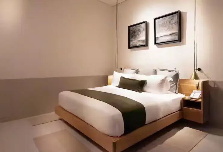Doppelbett mit Holzrahmen, weißer Bettwäsche und zwei Bildern an der hellen Wand.