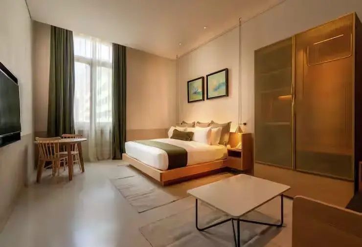 Helles Hotelzimmer mit Doppelbett, Couchtisch und kleiner Sitzgruppe am Fenster.