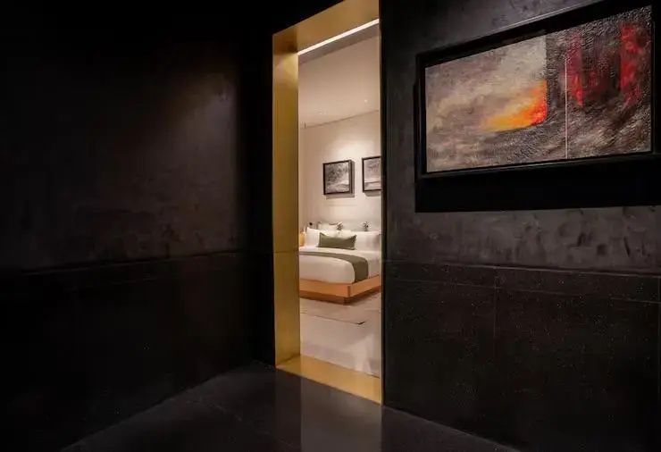 Blick durch einen dunklen Türrahmen mit goldener Kante auf ein helles Hotelzimmer mit Doppelbett.