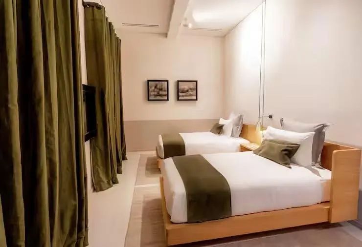 Hotelzimmer mit zwei Einzelbetten, grünen Läufern und langen Vorhängen an den Wänden.