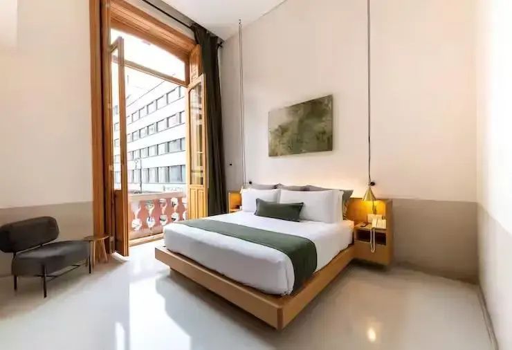 Helles Hotelzimmer mit Doppelbett, grüner Tagesdecke und hohem Balkonfenster.