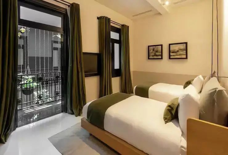 Helles Hotelzimmer mit zwei Einzelbetten, grünen Vorhängen und Balkon.