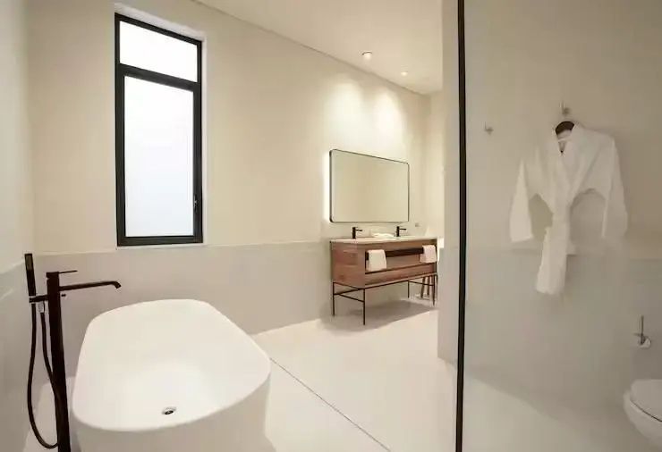 Modernes Badezimmer mit freistehender Badewanne, hölzernem Waschtisch und beleuchtetem Spiegel.