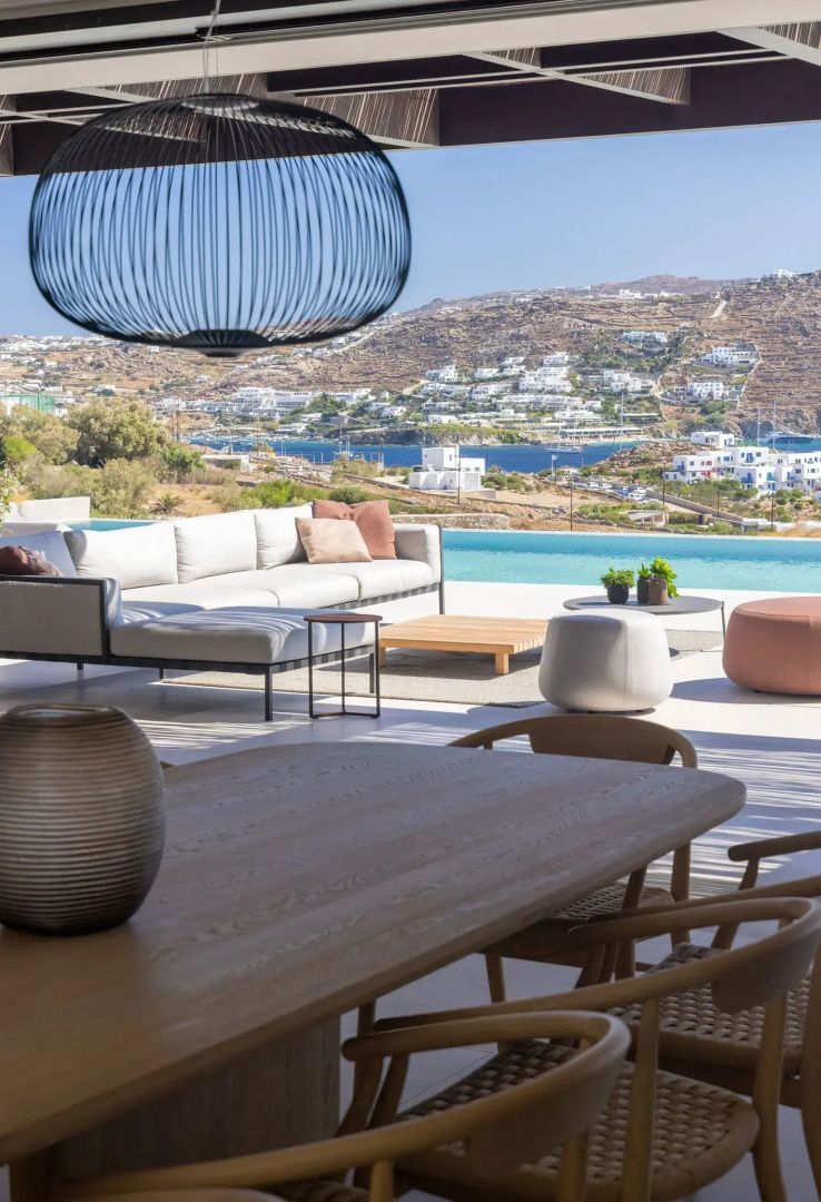 Terrasse mit Lounge-Möbeln und freiem Blick über den Pool auf eine Meeresbucht.