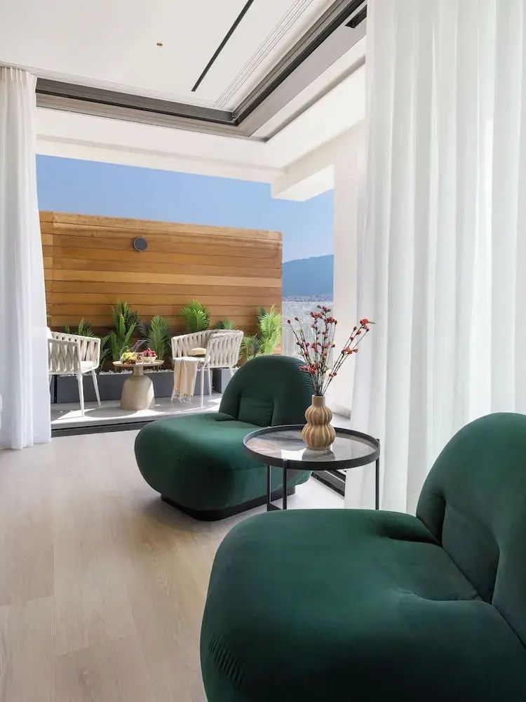 Wohnbereich im Zimmer mit zwei grünen Sesseln und Blick auf die angrenzende Terrasse.