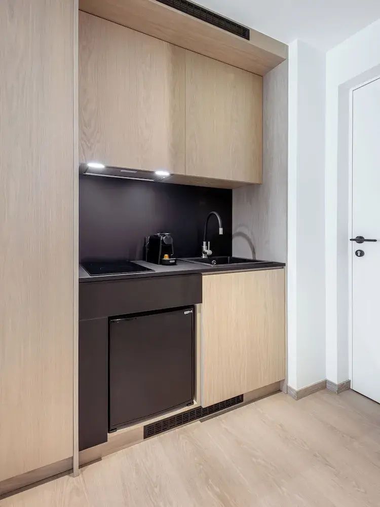 Kleine Küchenzeile aus Holz und Schwarz mit Spülbecken, Kaffeemaschine und integriertem Minikühlschrank.