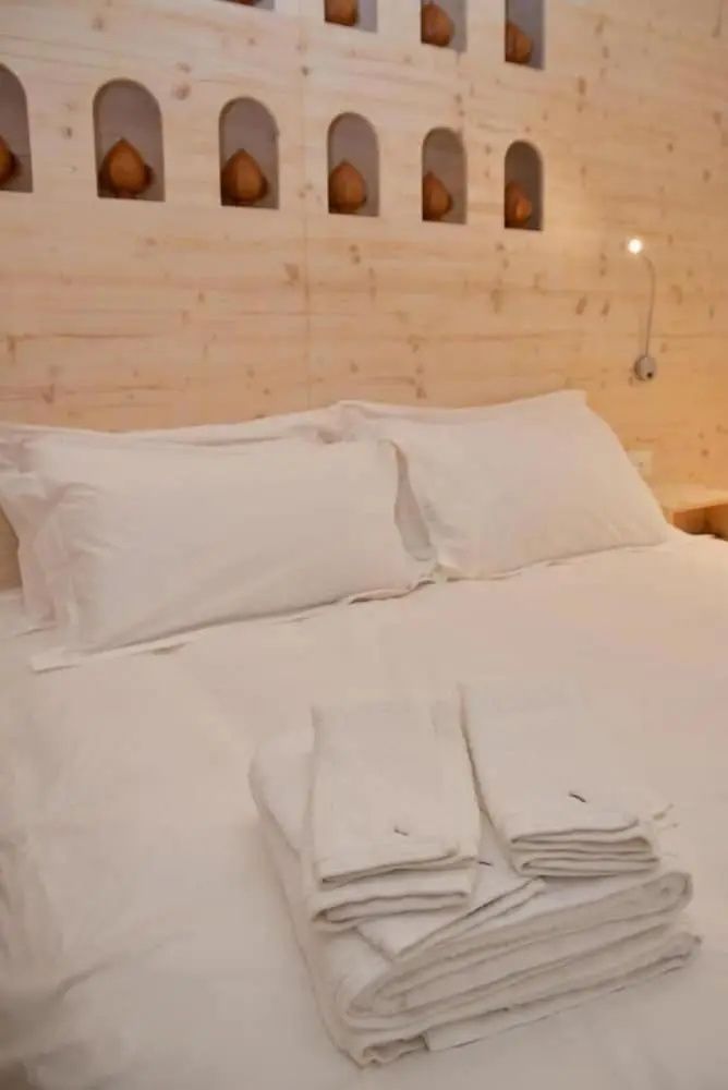 Ein gemachtes Doppelbett mit weißer Bettwäsche und Handtüchern vor einer hellen Holzwand.
