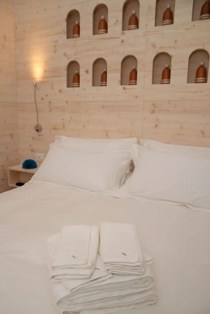 Doppelbett mit weißen Kissen vor einer Wand aus hellem Holz mit kleinen Nischen.