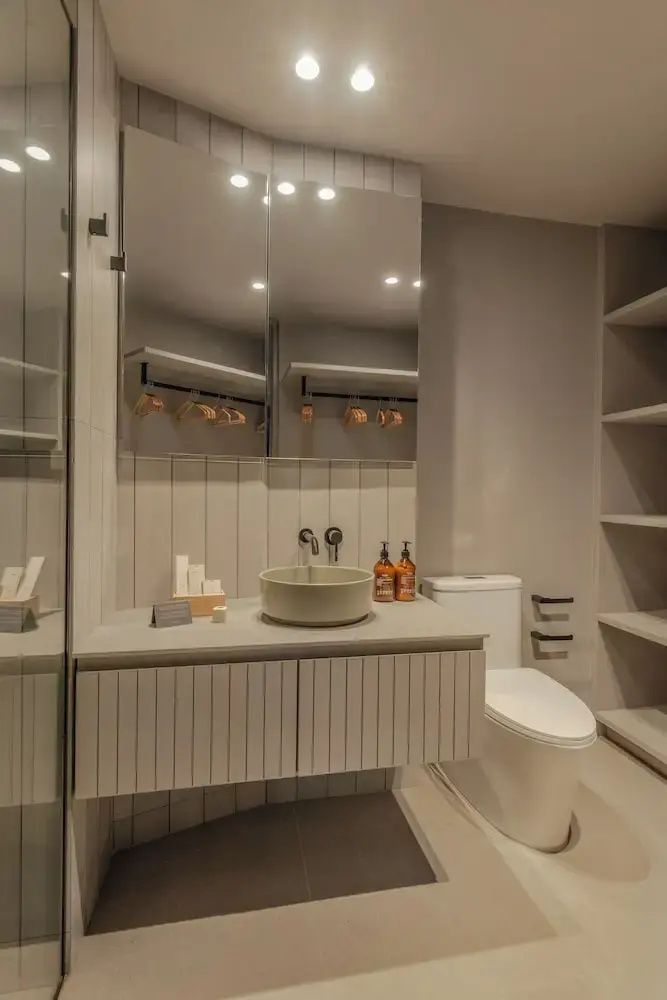 Badezimmer mit hellem Waschtisch, Spiegelschrank, rundem Waschbecken und Toilette.